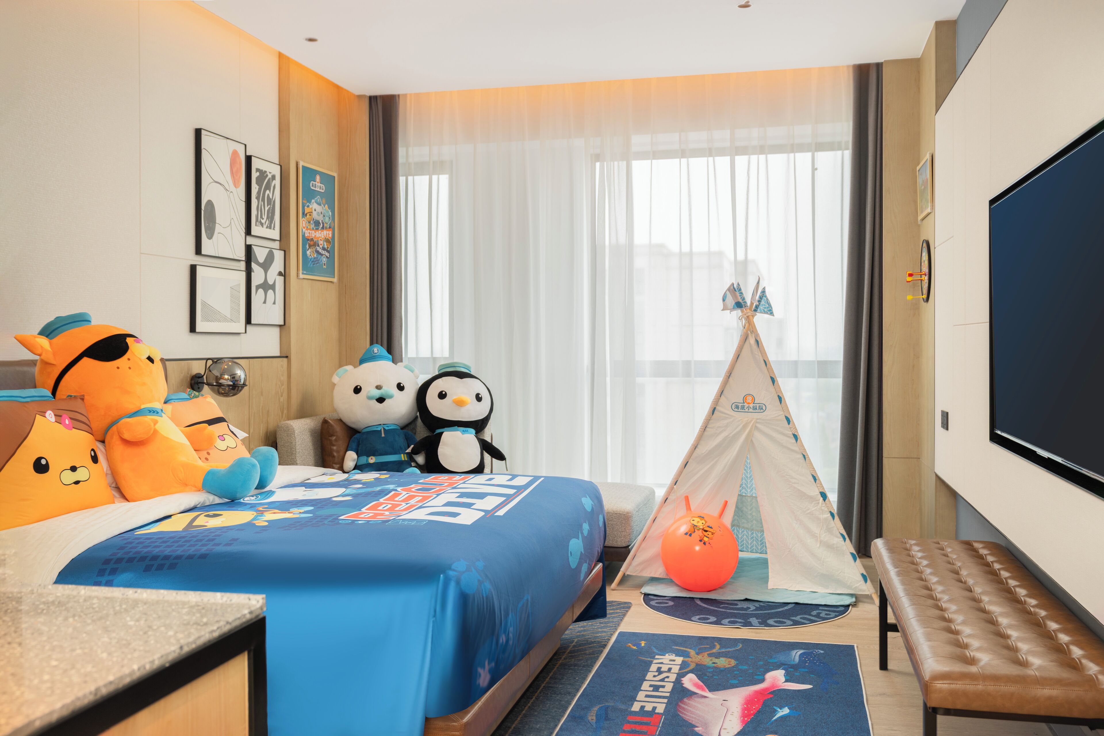 Una habitación de hotel con cama, una banca, una tienda de campaña y una gran pantalla de televisión.