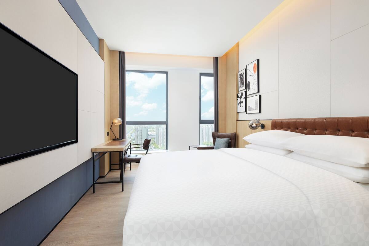 A modern hotel room with a large bed, a desk, and a TV.