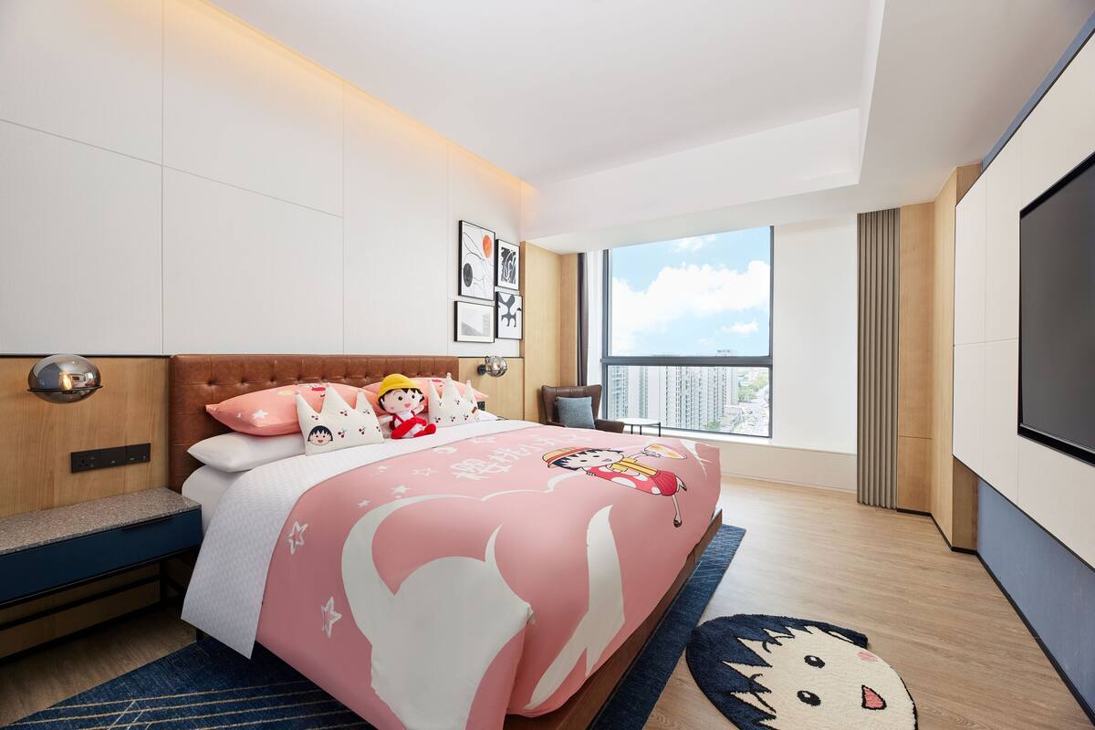 A modern hotel room with a large bed, a TV, a balcony, and a city view.