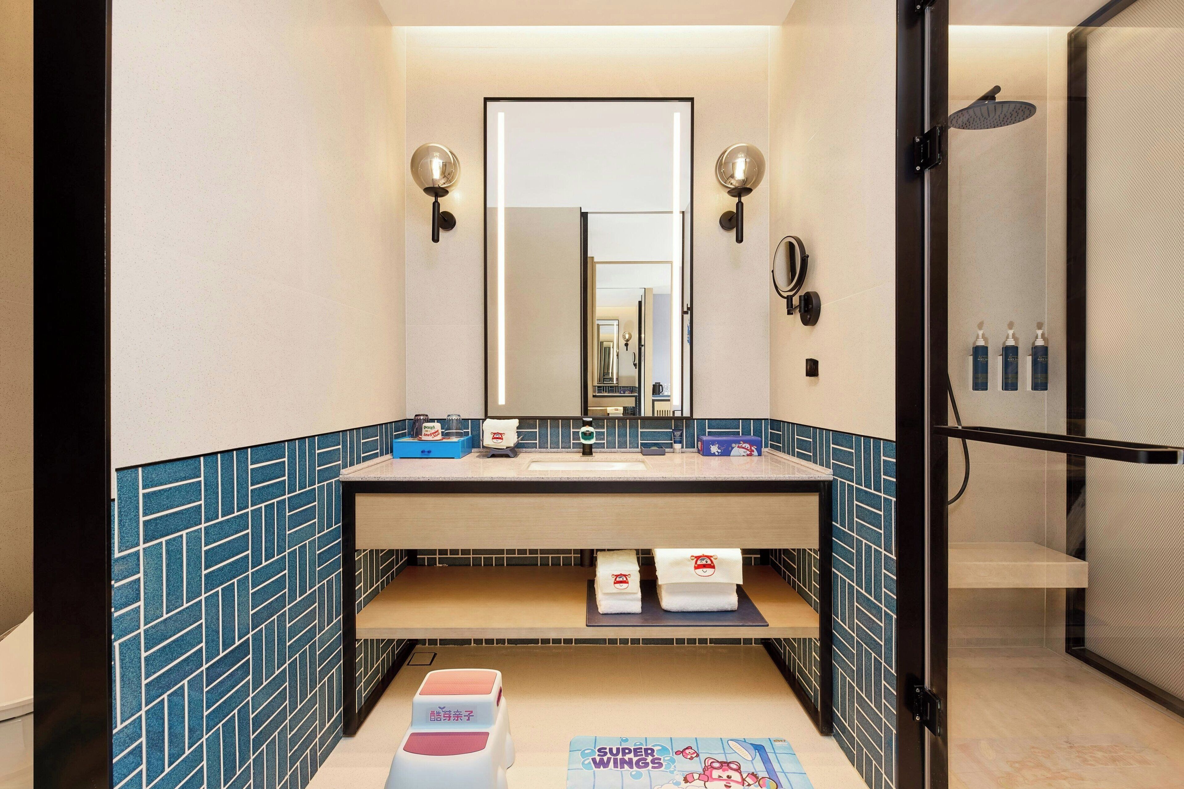 A modern bathroom with a large mirror, two wall sconces, a shower area, and a towel rack.