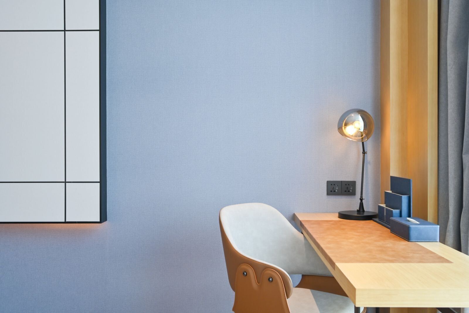 Una habitación de hotel moderna con un escritorio de madera, una silla blanca, una lámpara de pared y un mueble azul.