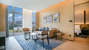 Una habitación de hotel moderna con un gran ventanal, un sofá, dos sillones, una mesita y una mesita de noche con lámpara.