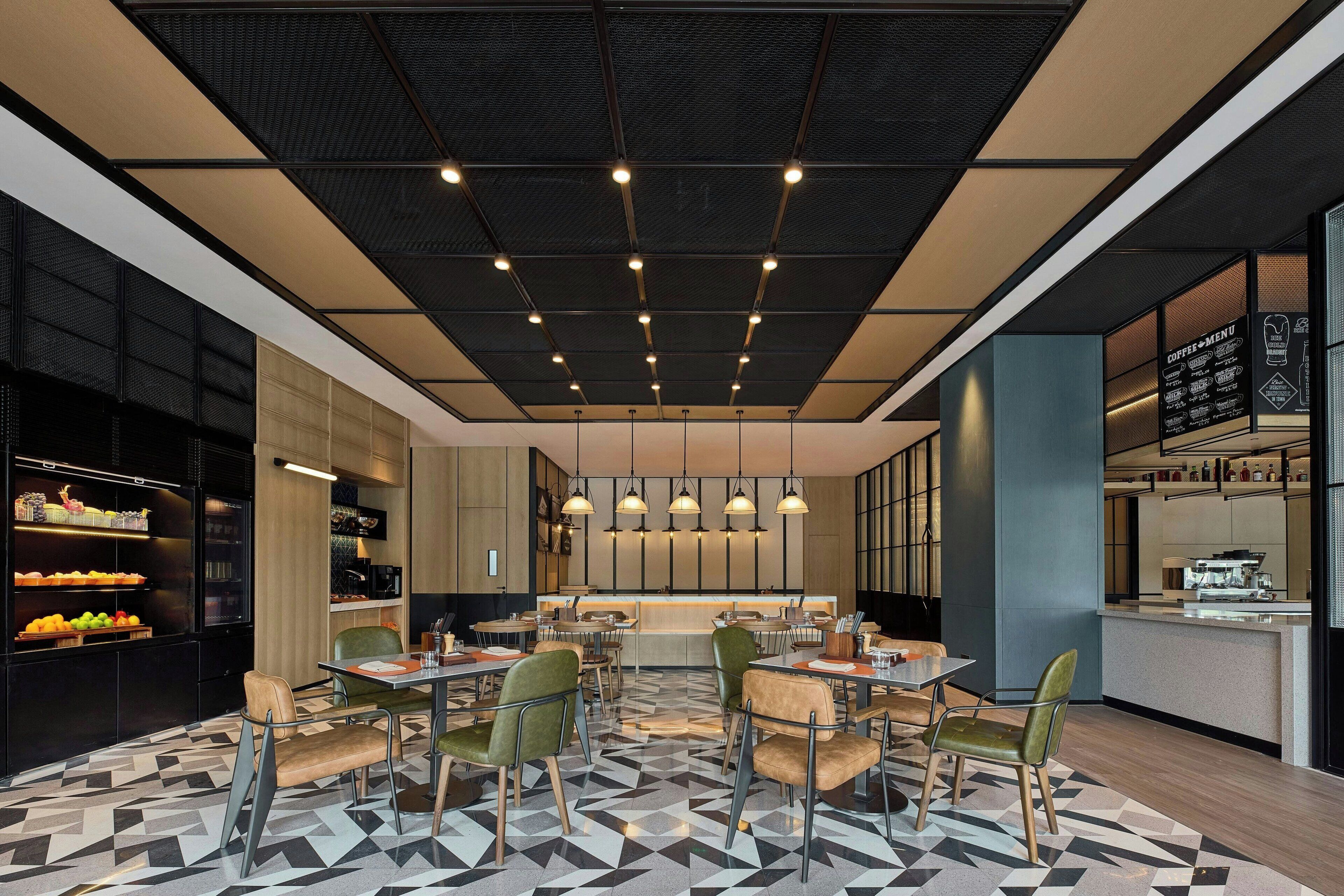 A modern restaurant with a geometric patterned floor, a central dining area with tables and chairs, and a kitchen visible through a glass partition.