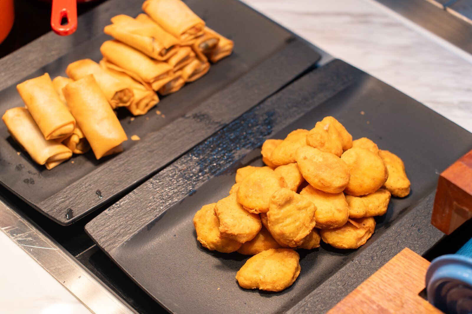 A kitchen counter with two trays of food items, one with rolled items and the other with fried items.