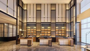 Un moderno vestíbulo de hotel con una recepción central, ventanas amplias y un suelo de mármol.