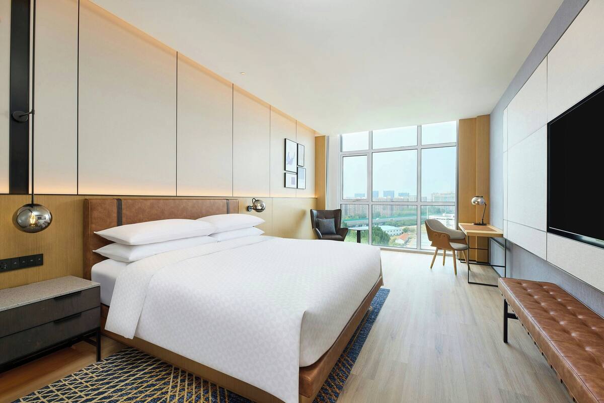 A modern hotel room with a large bed, a desk, a chair, and a TV.