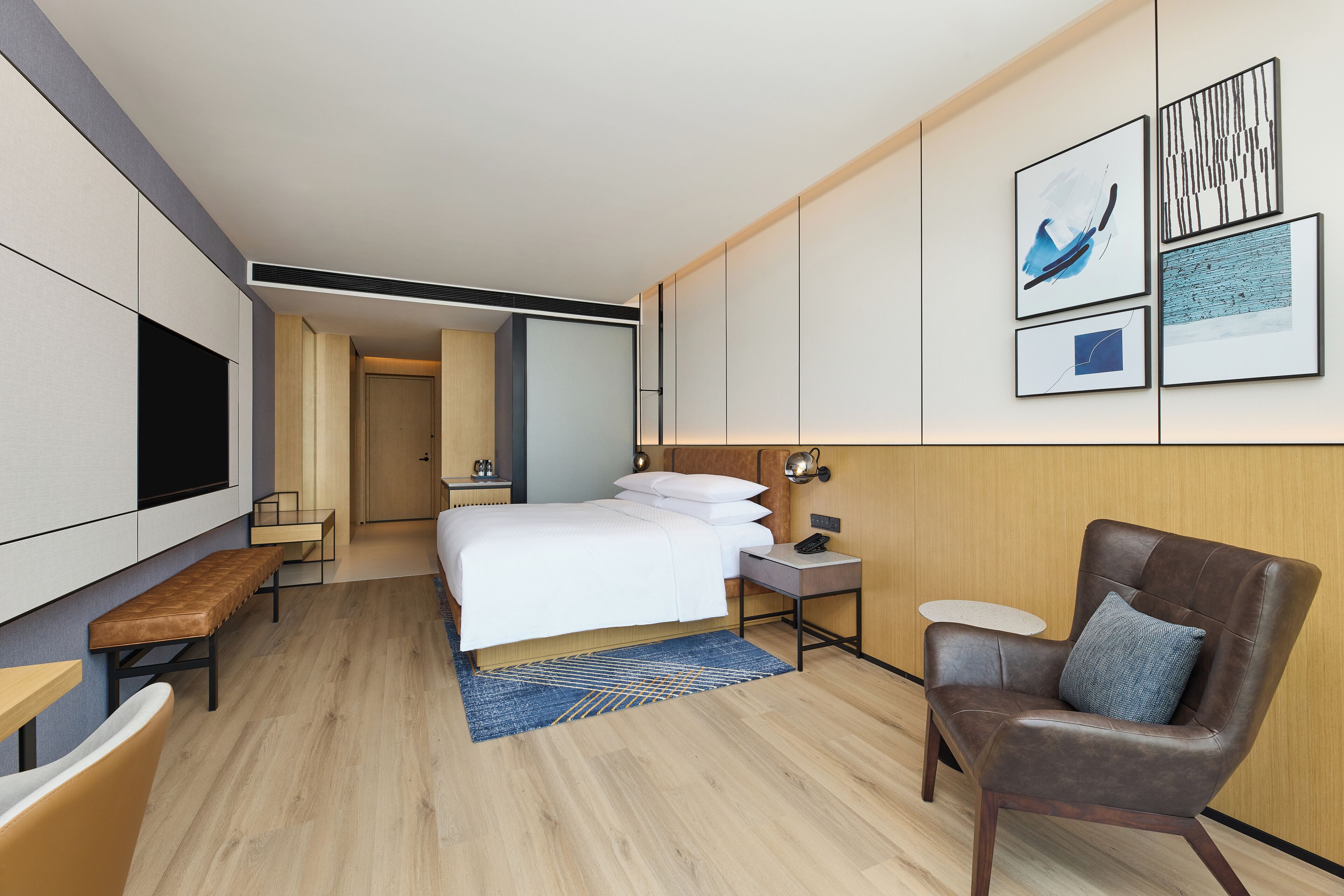 Ein modernes Hotelzimmer mit einem großen Bett, einem Schreibtisch, einem Stuhl, einem Fernseher und Kunstwerken an der Wand.