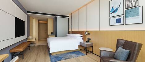 Ein modernes Hotelzimmer mit einem großen Bett, einem Schreibtisch, einem Stuhl, einem Fernseher und Kunstwerken an der Wand.