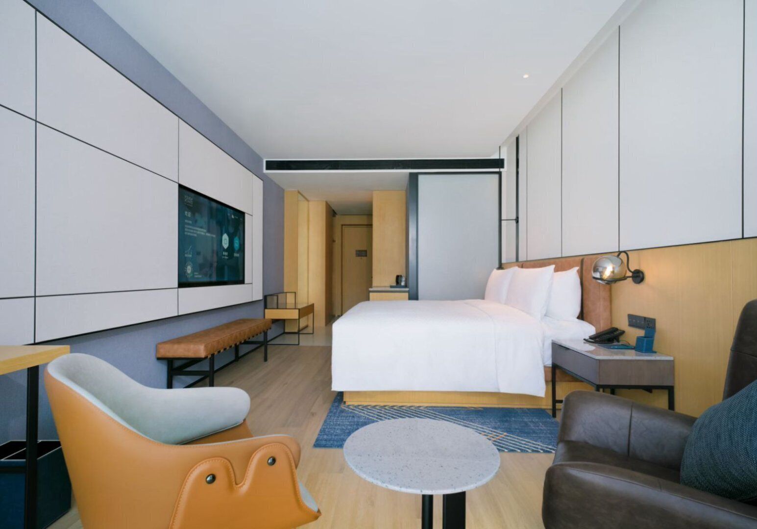 Une chambre d’hôtel moderne avec un grand lit, un bureau avec une lampe, une chaise et une petite table.