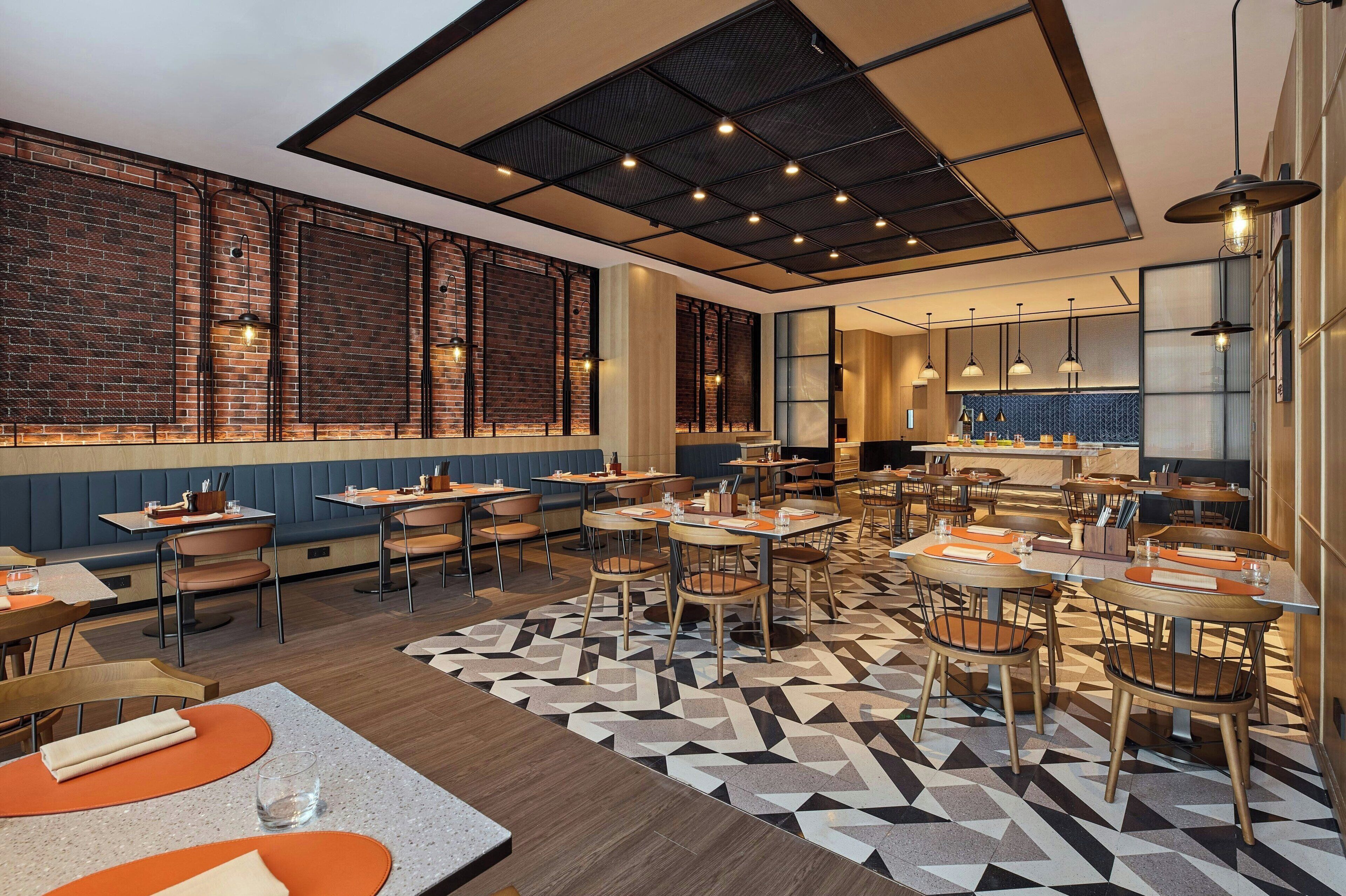 A restaurant with a modern interior, featuring brick walls, wooden tables, and a geometric patterned floor.