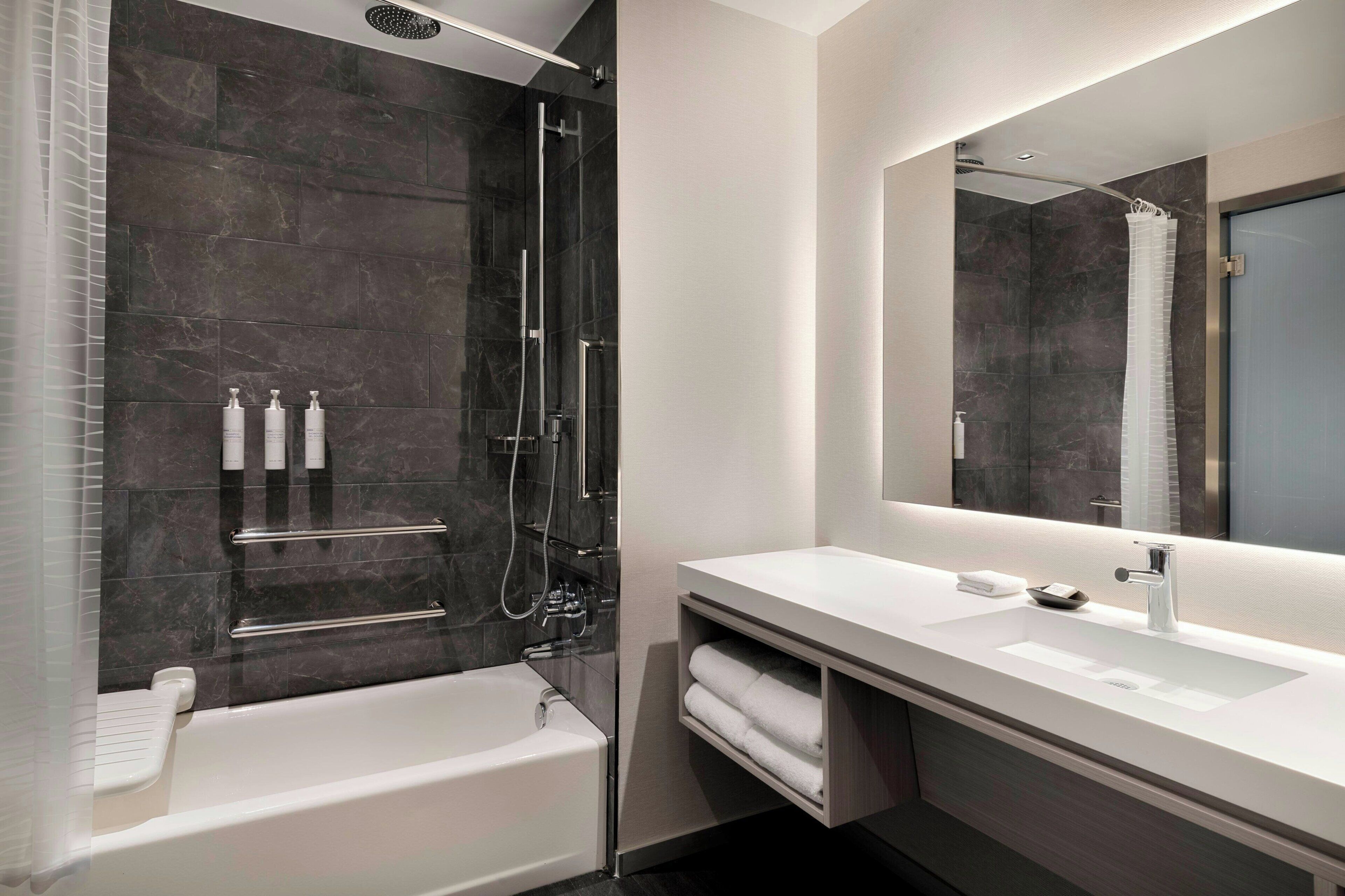 A modern bathroom with a bathtub, a walk-in shower, a large mirror, and a vanity with a sink.