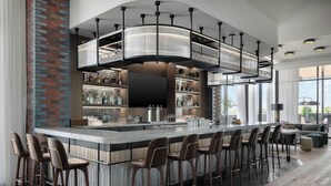 A modern bar area with a long counter, multiple stools, and a large overhead light fixture.