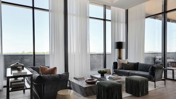 A modern living room with a sofa, ottoman, coffee table, and a side table with books and a lamp.