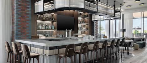 A modern bar area with a long counter, multiple stools, and a large overhead light fixture.