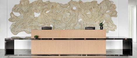 Een receptiebalie met een modern ontwerp, een groot abstract kunstwerk erboven en een kleine potplant aan de rechterkant.