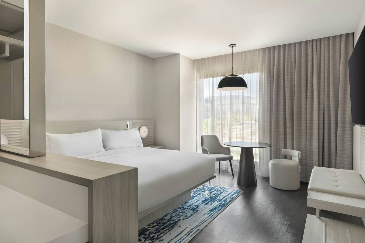 Quarto de hotel moderno com uma cama grande, uma escrivaninha, uma cadeira e um sofá.