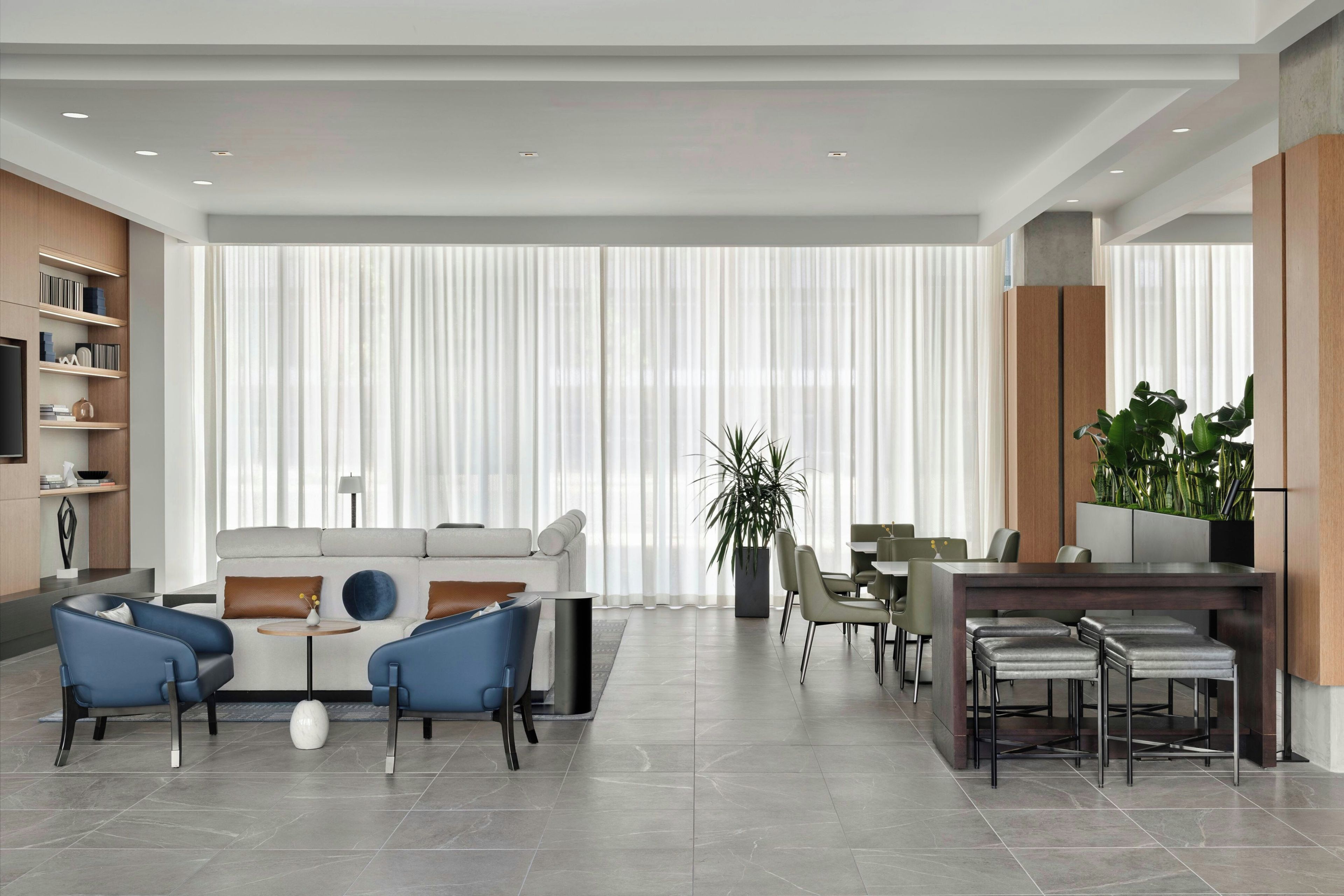 Una sala de estar moderna con sofá, sillas, zona de comedor y un amplio ventanal con cortinas.