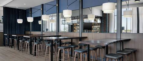 A modern bar area with multiple stools, a long counter, and pendant lighting.