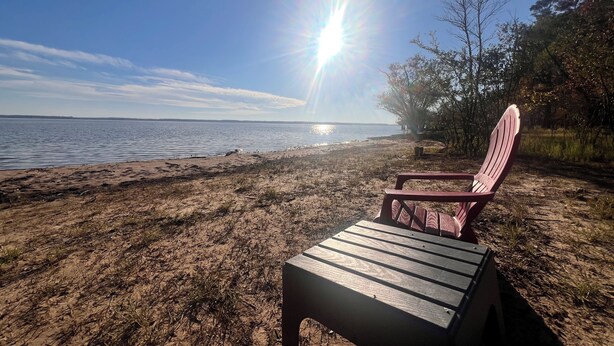 A beach with a wooden chair and a wooden table, a clear sky, and the sun shining. - Cozy fisherman cabin step from Lake Sam Rayburn (Etoile)