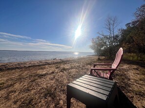 A beach with a wooden chair and a wooden table, a clear sky, and the sun shining.