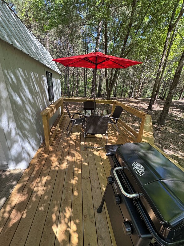 A wooden deck with a grill, chairs, and a red umbrella.
