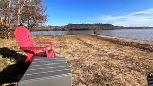A red Adirondack chair by a lake with a clear view of the water and trees in the background. - Cozy fisherman cabin step from Lake Sam Rayburn (Etoile)