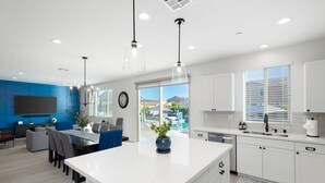 Une cuisine moderne avec des meubles blancs, un grand îlot central et des luminaires suspendus.