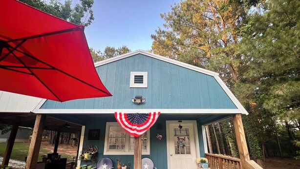 Un bâtiment bleu avec un porche, un parasol rouge et un paillasson.