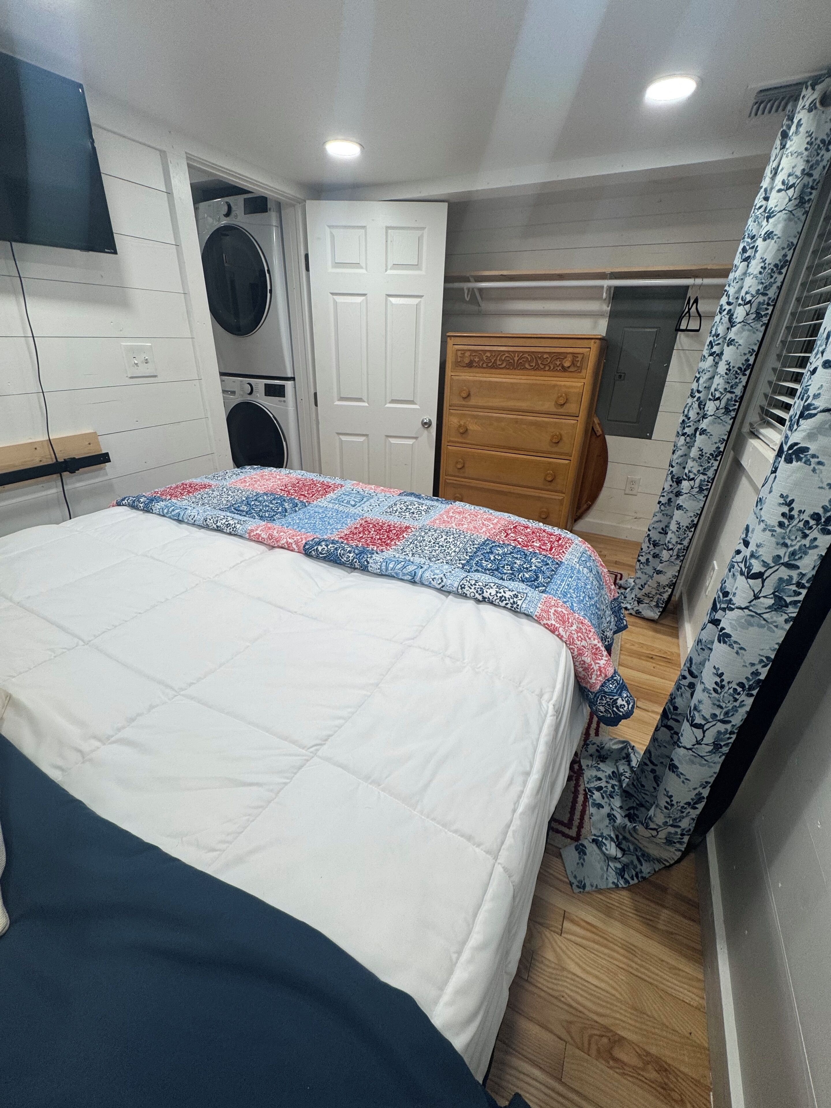 Een slaapkamer met een bed, een houten dressoir, een wasmachine en een deur.