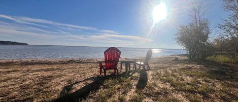 Ein Strand mit einem roten Adirondack-Sessel und einem Tisch, einem klaren Himmel und strahlender Sonne.