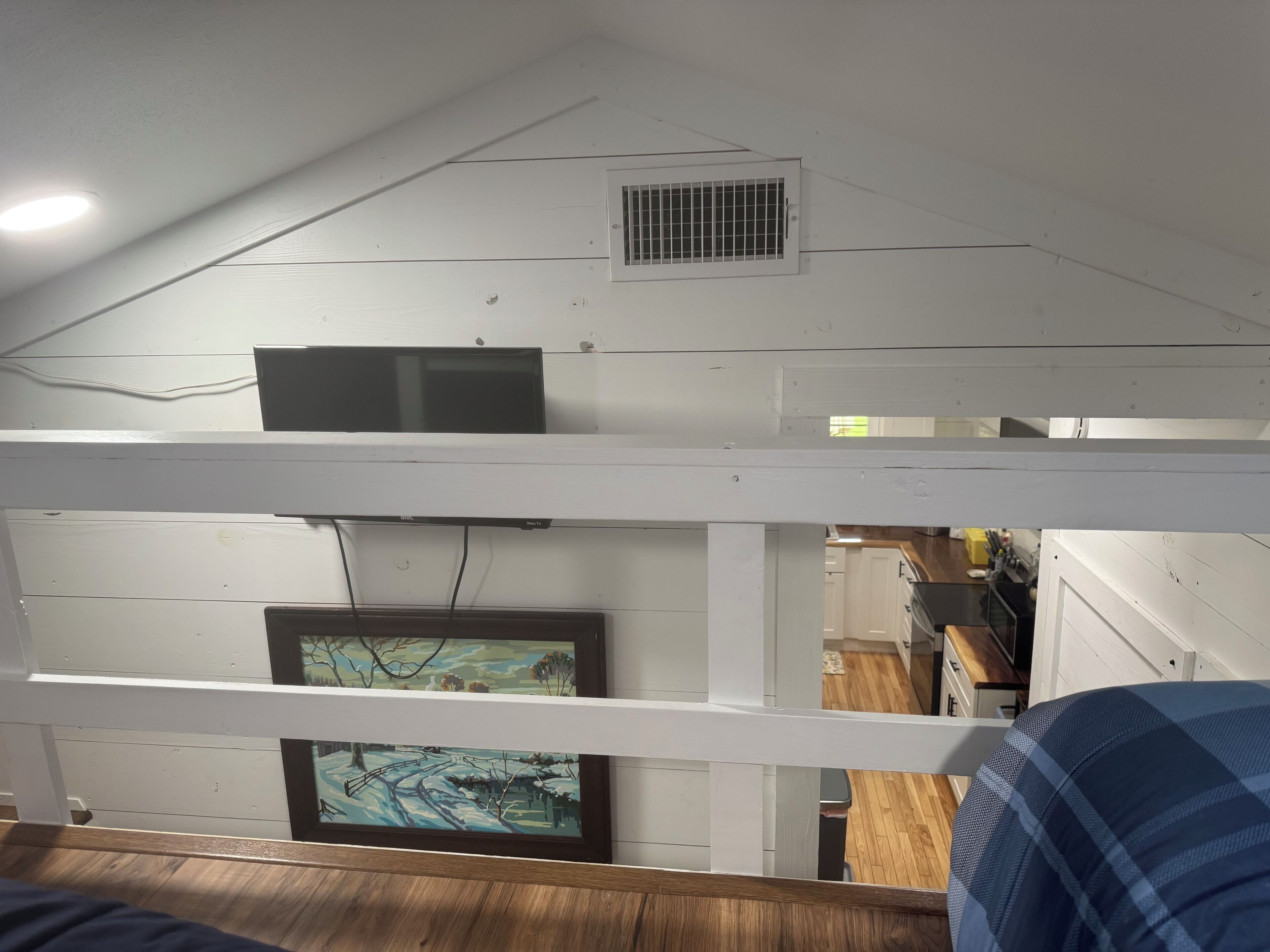 Een kamer met een stapelbed, een plafondventilator, een ventilatieopening en een ingelijst schilderij aan de muur.