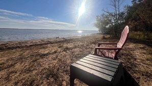 Une plage avec une chaise en bois et une table en bois, un ciel dégagé et un soleil éclatant.