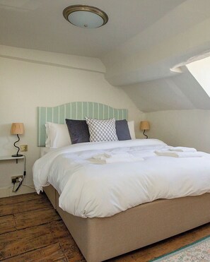 A bedroom with a bed, bedside lamps, a power outlet, and a wooden floor.