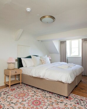 A bedroom with a bed, a nightstand, a lamp, a ceiling light, a window with curtains, and a patterned rug.