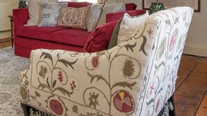 Een woonkamer met een rode bank, een fauteuil met patroon en een groot raam met gordijnen.