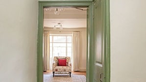 Een hal met een houten vloer, een groene deur en een gestreept fauteuil met een rode kussen.