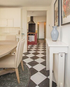 A kitchen with a checkered floor, a dining table, chairs, a stove, and a vase on a side table.