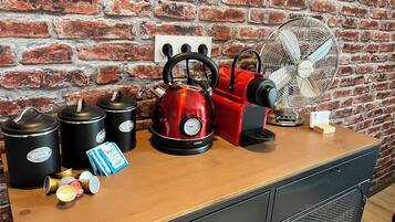 A kitchen counter with a red kettle, black kettles, a fan, and a coffee machine.
