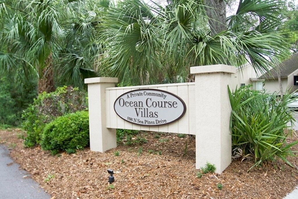 Schild für Ocean Course Villas, eine private Wohnanlage, mit freiem Blick auf die umgebende Grünfläche und einem gepflasterten Weg.