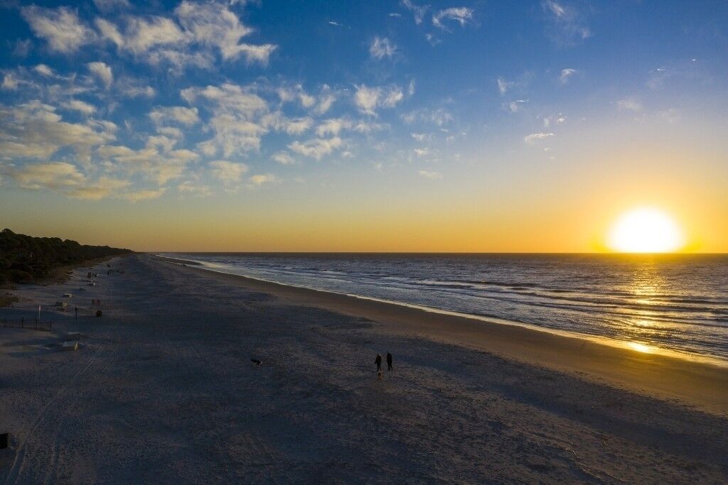 Une plage au coucher du soleil, avec des gens qui se promènent et un chien.