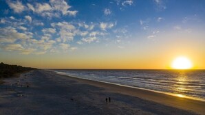 Une plage au coucher du soleil, avec des gens qui se promènent et un chien.