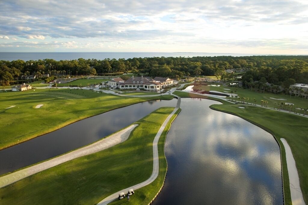 Un parcours de golf doté d’un grand étang, d’un club-house et entouré de verdure.