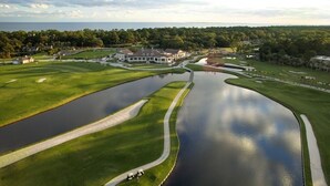 Un parcours de golf doté d’un grand étang, d’un club-house et entouré de verdure.