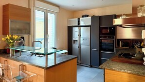Une cuisine moderne dotée d’un îlot central, d’appareils électroménagers en acier inoxydable et d’une table à plateau en verre.