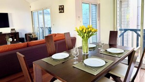 Un coin repas avec une table en bois dressée pour deux personnes, un canapé et un vase rempli de fleurs jaunes.