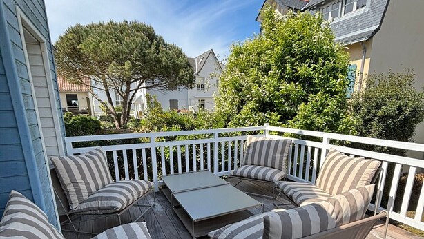 Une terrasse dotée d’une rambarde blanche, de sièges rembourrés et d’une table plate.