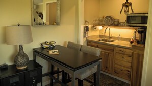 A compact kitchen with a sink, microwave, and a decorative bottle opener. A dining table with chairs is positioned in front of the kitchen. - Kiler Studio Apartment is a relaxing and charming wine country getaway for two! (Paso Robles)