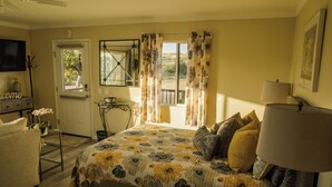 A bedroom with a bed, a bedside lamp, a small table with a bowl, a chair, and a TV on a stand. - Kiler Studio Apartment is a relaxing and charming wine country getaway for two! (Paso Robles)