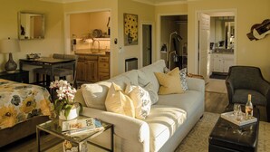 A well-lit living room with a sofa, coffee table, and a dining area with a kitchen in the background. - Kiler Studio Apartment is a relaxing and charming wine country getaway for two! (Paso Robles)