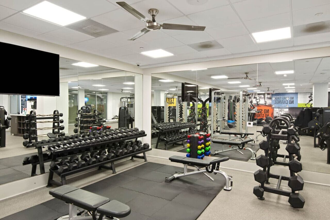 Ein Fitnessstudio mit unterschiedlicher Ausstattung, zum Beispiel Kurzhanteln, Bänken und Kraftgeräten.